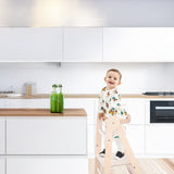 A Happy toddler standing on learning tower in the kitchen.